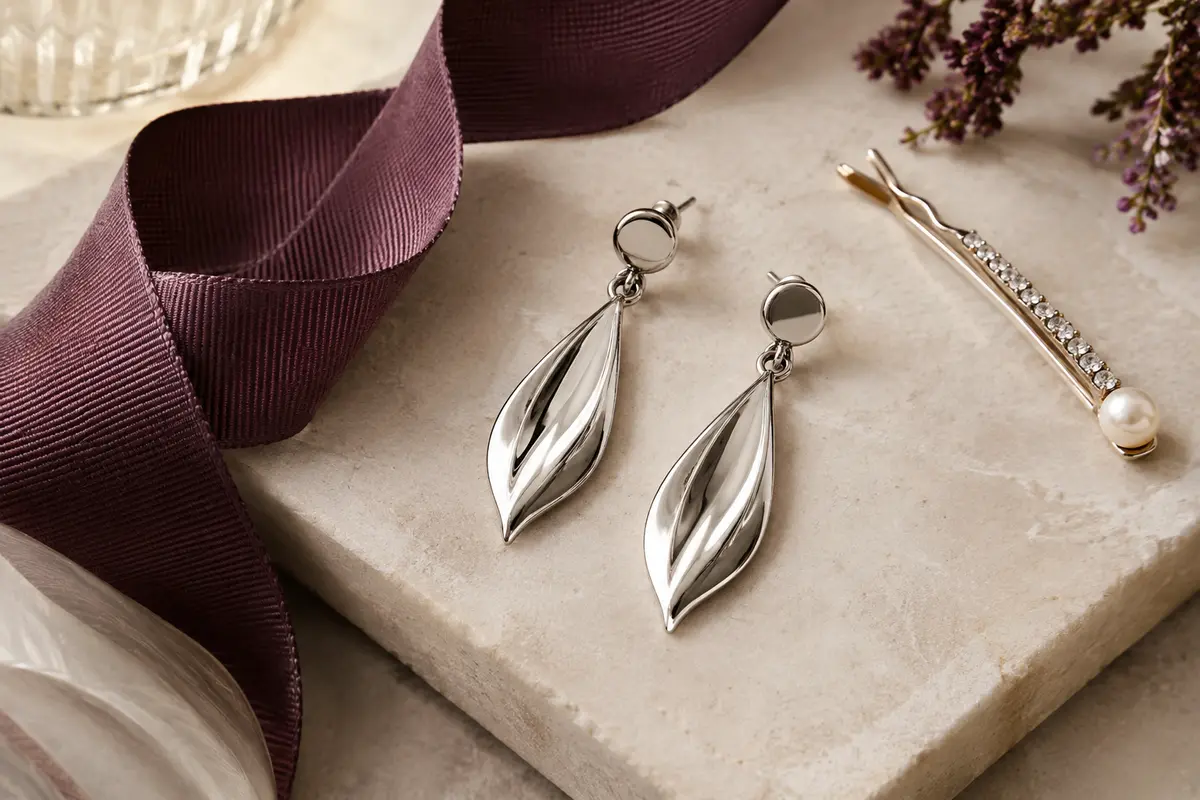 Boucles pendantes en acier posées près d’un tissu travaillé et d’une épingle à cheveux