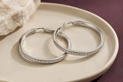 Paire de grandes créoles argentées ornées de zircones cubiques, posées sur un plateau en céramique ivoire.