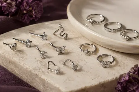 Clous et anneaux de nez argentés aux motifs variés, disposés sur une pierre claire avec des détails transparents.
