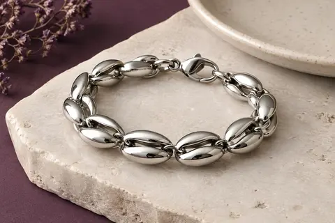 Bracelet argenté à maillons grain de café posé sur une pierre claire près d’un plateau en céramique.
