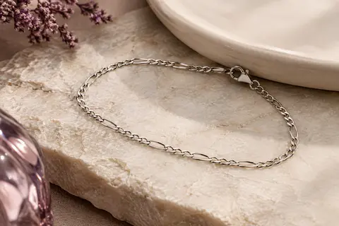 Chaîne de cheville Figaro fine en acier inoxydable argenté, disposée sur une pierre claire.