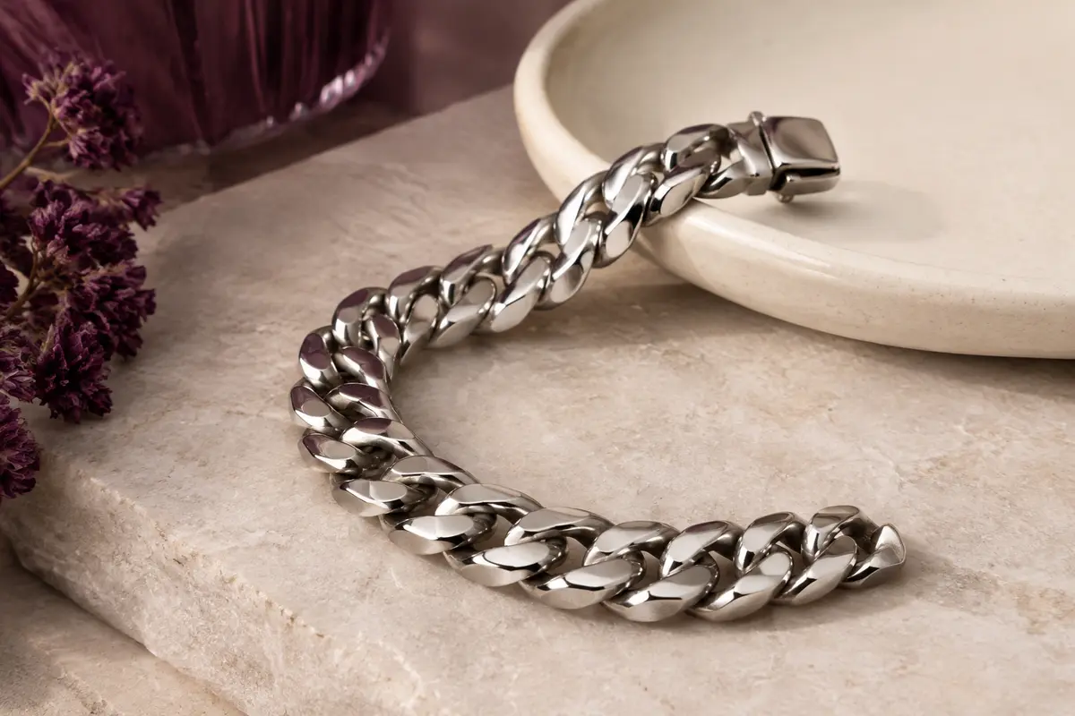 Bracelet chaîne Cuban en acier inoxydable poli, posé en courbe sur une pierre claire