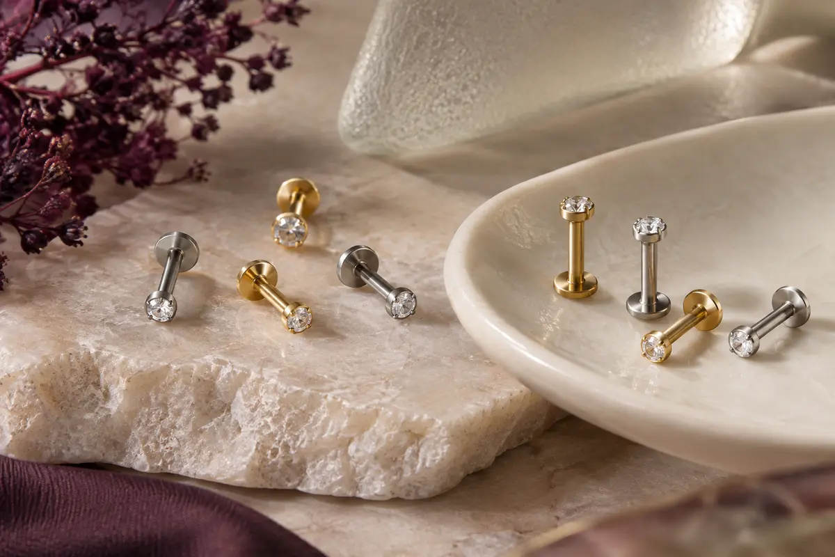 Labrets de piercing dorés et argentés ornés de petits zircons cubiques, disposés sur une pierre claire