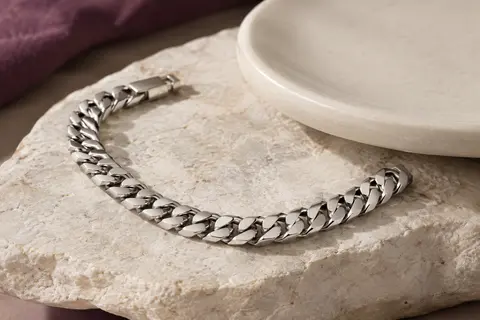 Bracelet chaîne cubaine argenté à maillons plats, posé en courbe sur une pierre claire