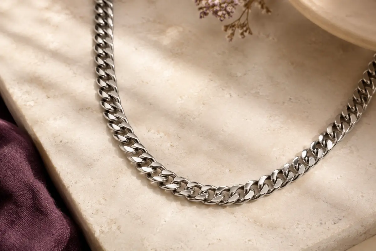 Collier ChainsHouse argenté à maillons cubains de 6 mm disposé en courbe sur une pierre claire.