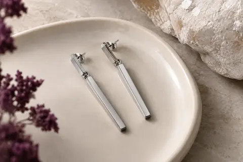 Paire de boucles d’oreilles pendantes géométriques argentées posées sur un plateau en céramique claire