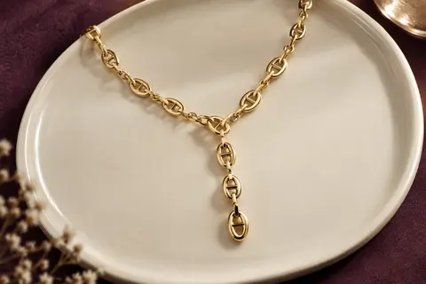 Collier doré en Y à maillons marins posé sur un plateau en céramique ivoire