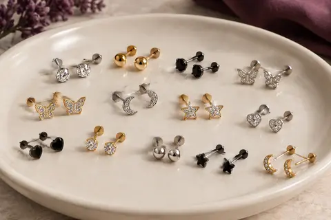 Assortiment de boucles d’oreilles à dos plat aux motifs variés, posé sur un plateau en céramique ivoire.