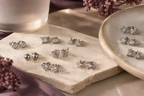 Puces d’oreilles argentées aux formes variées, ornées de zircones cubiques et disposées sur une pierre claire.