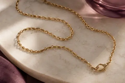 Chaîne dorée fine à maillons Rolo disposée en boucles sur une surface claire