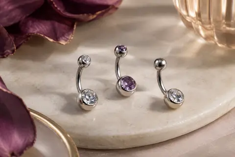 Trois piercings de nombril courts argentés à zircons, disposés sur une surface claire