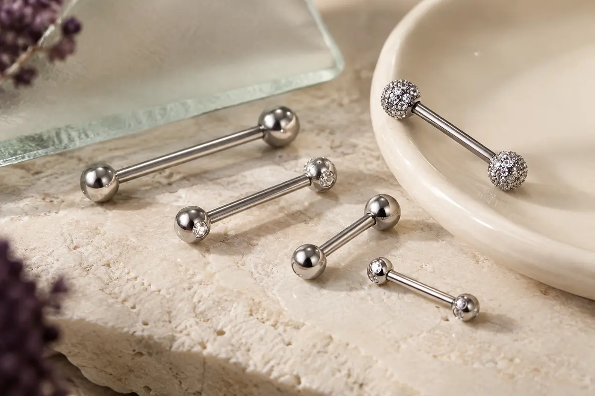 Barbells droits argentés à boules brillantes et détails en zircon cubique, posés sur une pierre claire.