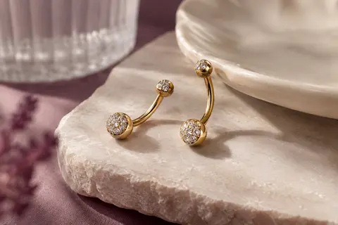 Barbells courbés à l’aspect doré et au pavé de zircon cubique disposés sur une pierre claire