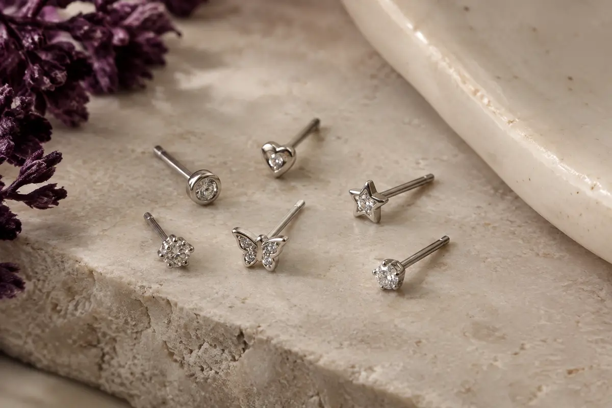 Lot de 21 piercings de nez argentés à motifs de cœur, étoile, papillon et zircone, disposés sur pierre claire.