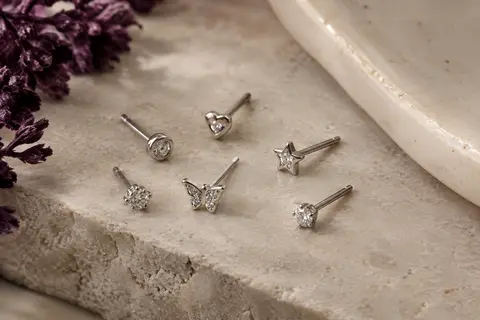 Lot de 21 piercings de nez argentés à motifs de cœur, étoile, papillon et zircone, disposés sur pierre claire.