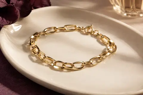 Bracelet chaîne doré à maillons ouverts et fermoir à ressort posé sur un plateau en céramique claire.