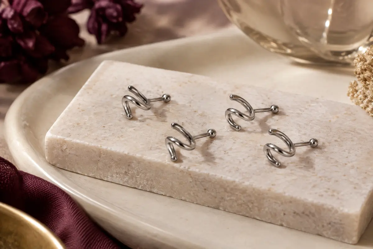 Quatre piercings de nez spirale en acier argenté disposés sur une pierre claire