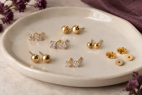 Petits clous d’oreilles ton or à zircon transparent et boule ronde disposés sur une céramique ivoire