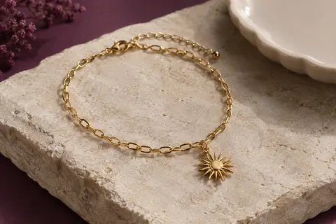 Bracelet de cheville doré à maillons ovales et pendentif soleil, posé sur une pierre claire.