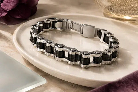 Bracelet Ostan à larges maillons noirs et argentés posé sur un plateau en céramique claire