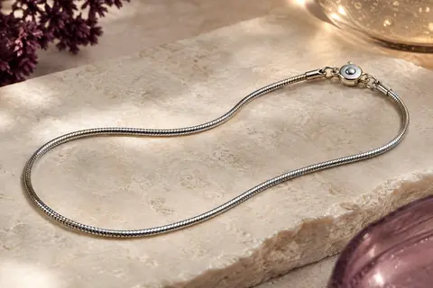 Chaîne argentée Prosteel à maille serpent fine, disposée en courbe sur une pierre claire
