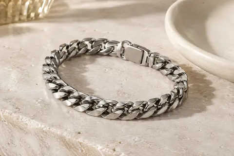 Bracelet gourmette cubaine argentée à maillons épais, disposé sur une pierre claire.