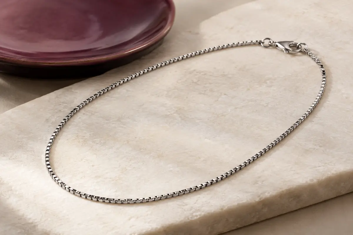 Collier argenté en acier inoxydable à chaîne boîte fine, posé en ovale sur une pierre claire