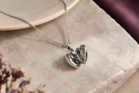 Collier argenté à médaillon cœur ouvert, posé sur une pierre claire avec deux photos visibles