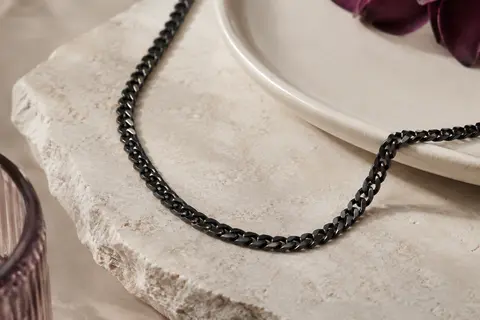 Collier chaîne cubaine noire à maillons de 4 mm posé sur une pierre claire près d’un plateau en céramique.