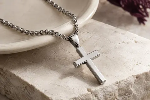 Collier argenté avec pendentif croix classique et chaîne en acier inoxydable posé sur une pierre claire