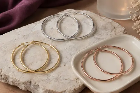 Trois paires de grandes créoles rondes en finitions argentée, dorée et or rose, disposées sur une pierre claire.