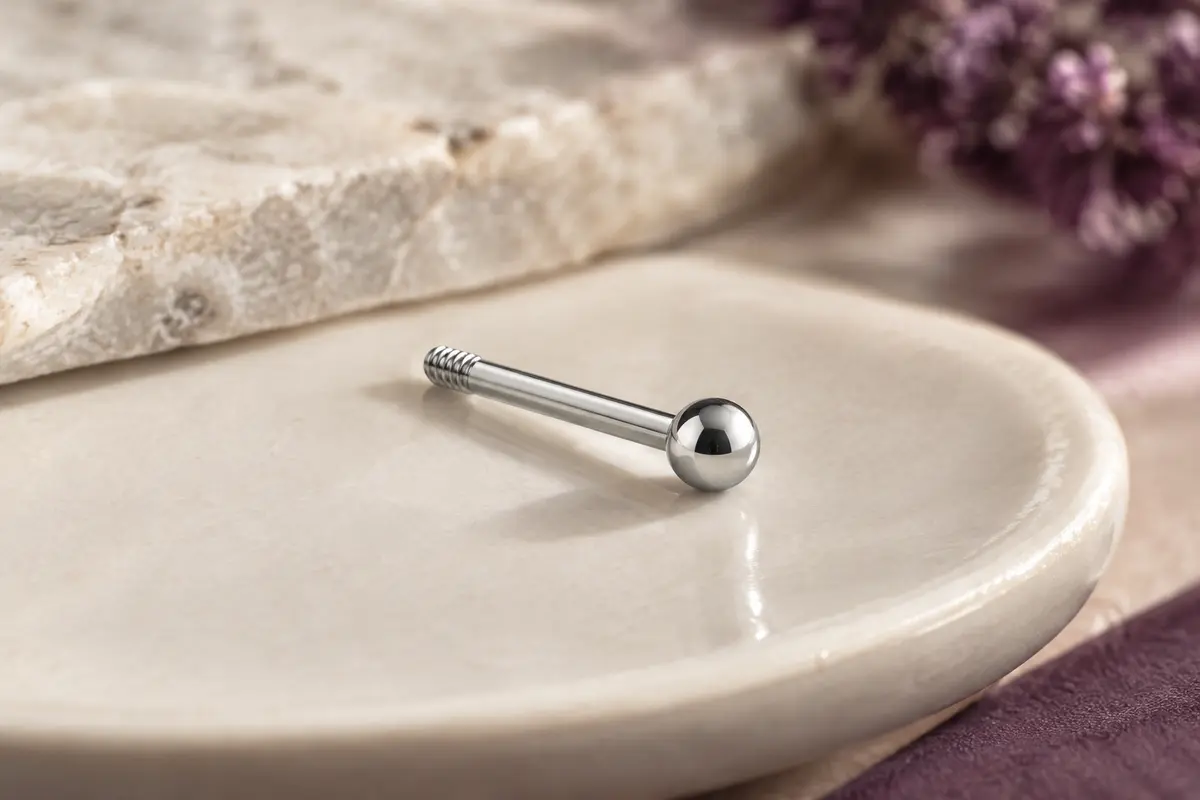Labret droit argenté à filetage externe et boule ronde, photographié sur un plateau en céramique ivoire.