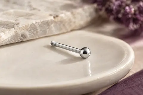 Labret droit argenté à filetage externe et boule ronde, photographié sur un plateau en céramique ivoire.