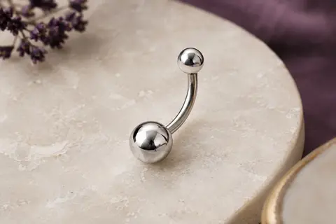 Piercing de nombril en forme de banane classique en acier, posé sur une céramique claire