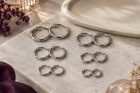 Six paires d’anneaux de piercing argentés à charnière, disposées sur une pierre claire