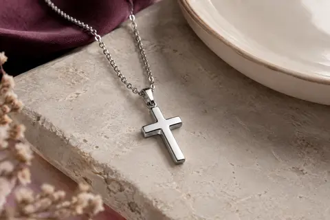 Collier argenté en acier inoxydable avec pendentif croix poli posé sur une pierre claire.